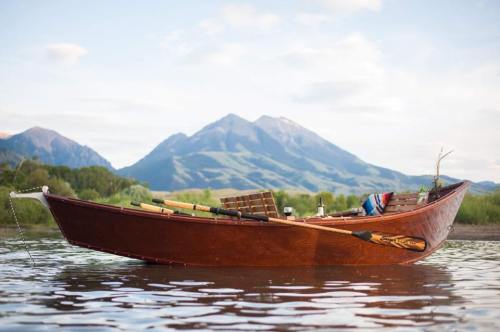 A wooden boat on calm water with mountains in the background under a clear sky.