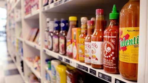 A shelf filled with various sauces and condiments in colorful bottles, showcasing a variety of brands and flavors.
