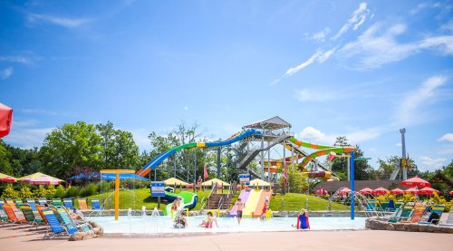 A vibrant water park scene with colorful slides, children playing in the water, and lounge chairs under a clear blue sky.