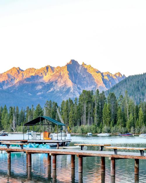 A serene lake scene with a wooden dock, a boat, and mountains in the background, illuminated by the sunset.