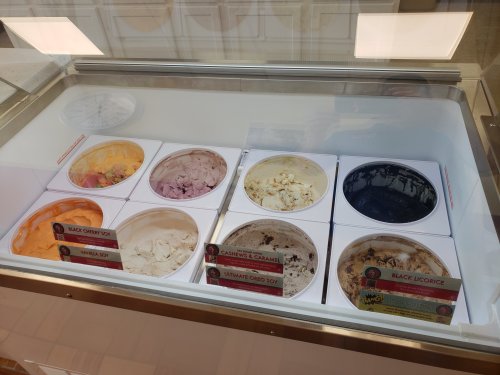 A display of eight ice cream tubs in a freezer, featuring various flavors like black cherry, vanilla, and black licorice.