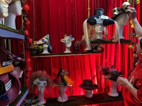A display of colorful hats on mannequin heads against a red backdrop, with a person adjusting a hat.