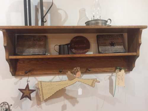 Wooden shelf displaying decorative items, including signs, a plate, and a whimsical angel figure with a tag.