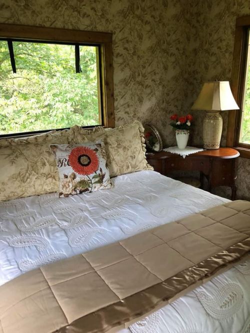 Cozy bedroom with floral wallpaper, a neatly made bed, decorative pillows, and a lamp on a bedside table.