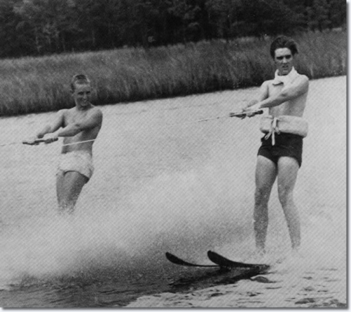 Two young men water skiing on a lake, creating splashes as they glide across the surface.