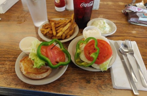 Two plates with burgers topped with lettuce, tomato, and bell pepper, served with fries and ice cream on the side.