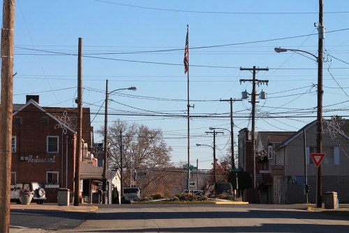 A quiet street scene with an American flag, utility poles, and buildings under a clear blue sky.