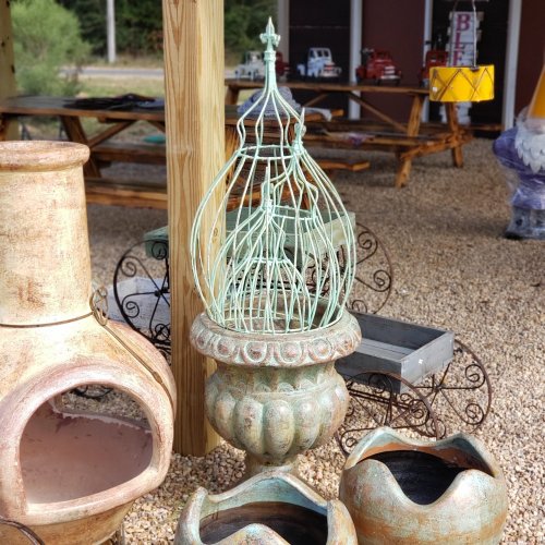 A decorative garden piece featuring a green metal cage atop a textured pot, surrounded by other rustic items.