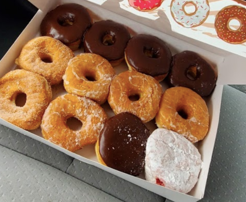 A box of assorted donuts, including chocolate-covered, powdered, and plain varieties, on a car seat.