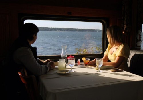 A couple sits at a table by a window, enjoying a meal with a scenic view of the water outside.