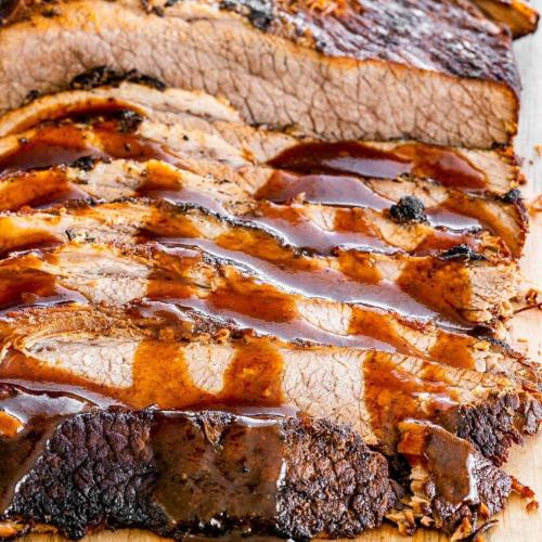 Sliced brisket drizzled with barbecue sauce on a wooden cutting board.