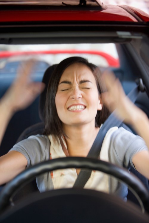 A frustrated woman grips the steering wheel, expressing anger while sitting in a car.