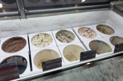 A display of various ice cream flavors in tubs, some nearly empty, with flavor labels visible.