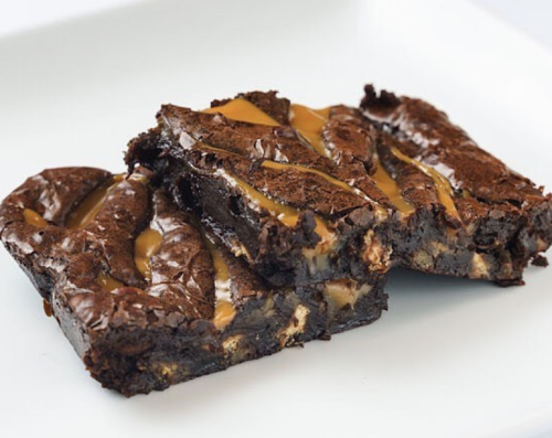 Two rich, fudgy brownies drizzled with caramel, cut into squares and placed on a white plate.