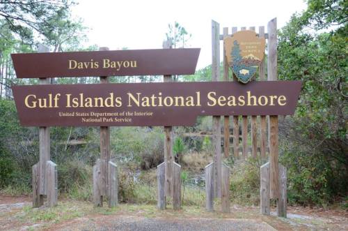 Sign for Davis Bayou at Gulf Islands National Seashore, featuring the National Park Service logo and surrounding greenery.