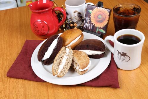 A plate of whoopie pies in chocolate and vanilla flavors, with coffee and iced tea on a wooden table.