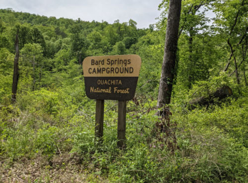 Sign for Bard Springs Campground in Ouachita National Forest, surrounded by lush green trees and vegetation.