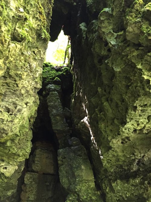 A narrow crevice between moss-covered rocks, with sunlight filtering through the top, illuminating the stone walls.