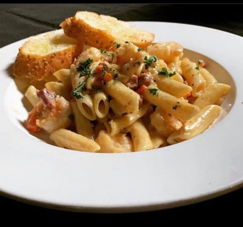 A plate of creamy pasta with shrimp and herbs, served with two slices of garlic bread.