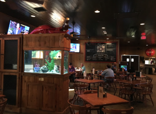Interior of a casual restaurant featuring wooden tables, an aquarium, and TVs showing sports.