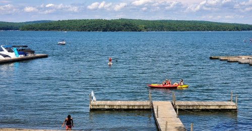 A serene lake scene with people kayaking and paddleboarding, surrounded by green hills and a clear blue sky.