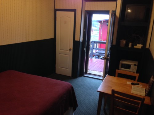 Cozy hotel room with a bed, small table, microwave, and door leading to a balcony.