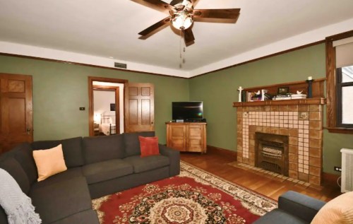 Cozy living room with a green wall, a large sofa, a patterned rug, and a fireplace with a wooden mantel.