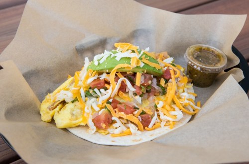 A taco filled with cheese, tomatoes, and avocado, served with a side of salsa in a paper-lined basket.