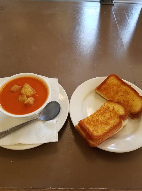 A bowl of tomato soup with croutons next to two slices of toasted bread on white plates.