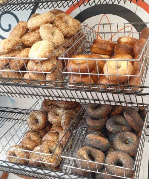 A display of assorted bagels in wire baskets, featuring sesame, plain, and darkly baked varieties.