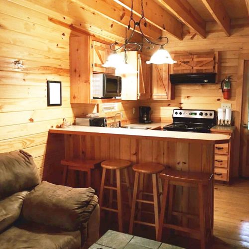 Cozy wooden kitchen with bar stools, microwave, stove, and a comfortable couch in a rustic cabin setting.