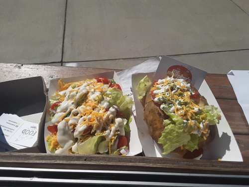 Two food containers: one with a colorful salad topped with cheese and dressing, the other with a loaded baked potato.