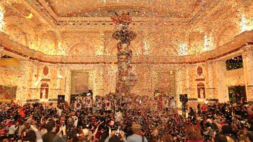 A lively celebration with colorful confetti falling in a grand hall filled with people enjoying the event.