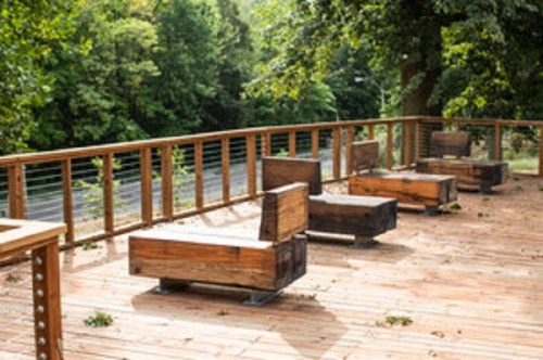 A wooden deck with several modern benches overlooking a green landscape and a road in the background.