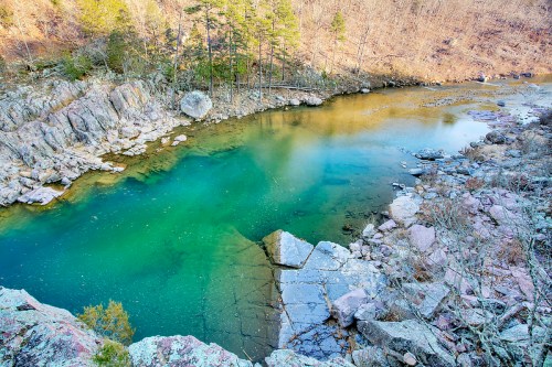 A serene river flows through rocky terrain, surrounded by trees and a steep, barren hillside.
