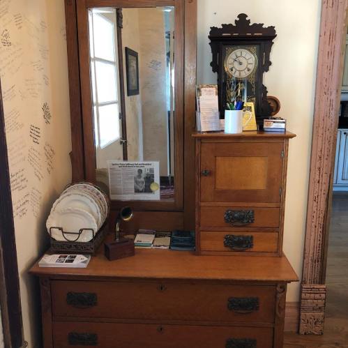 A wooden dresser with a mirror, clock, and various items on top, set against a wall with handwritten notes.
