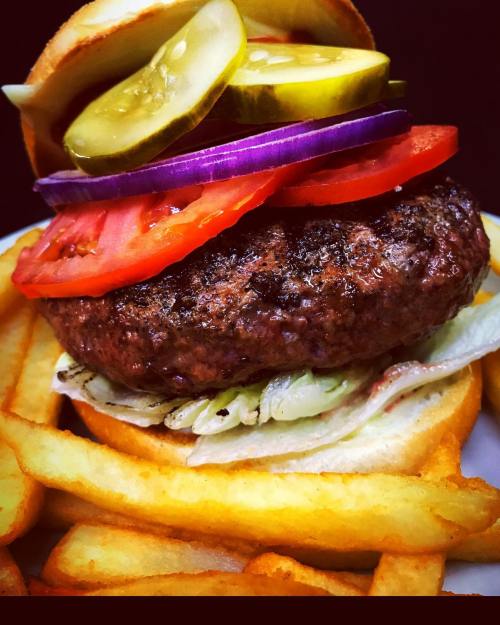 A juicy hamburger topped with lettuce, tomato, pickles, and onion, served with crispy French fries on the side.