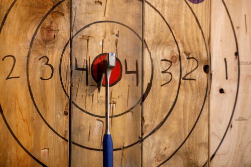 A close-up of a wooden target with a dart embedded in the red bullseye, surrounded by numbered circles.