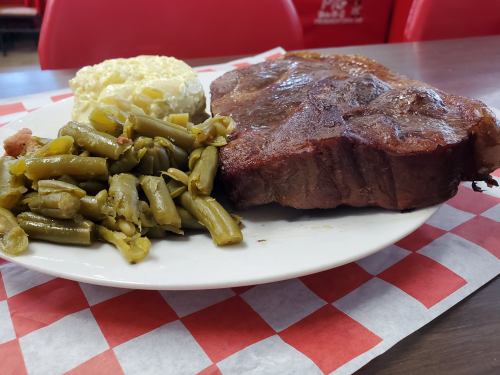 A plate featuring a large steak, green beans, and a serving of mashed potatoes on a checkered tablecloth.