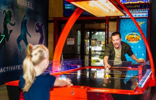 A man and a child play air hockey in an arcade, smiling and enjoying their game together.