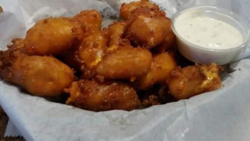 A basket of golden-brown fried snacks served with a small cup of dipping sauce.