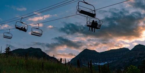 Silhouetted ski lift chairs against a sunset sky, with mountains in the background and clouds scattered above.