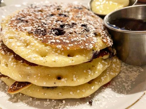 A stack of fluffy pancakes dusted with powdered sugar, served with syrup and a small cup of butter.