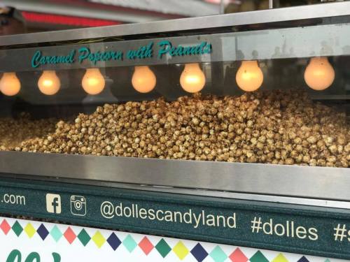 A popcorn stand displaying a large batch of caramel popcorn with peanuts, illuminated by string lights above.