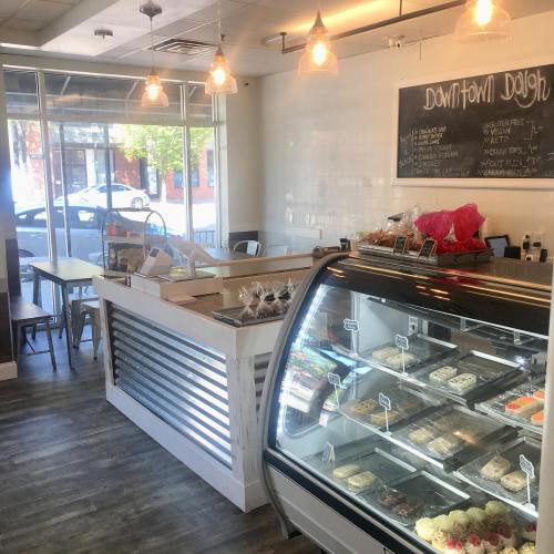 Bright café interior with a display case of desserts, a counter, and seating by large windows.