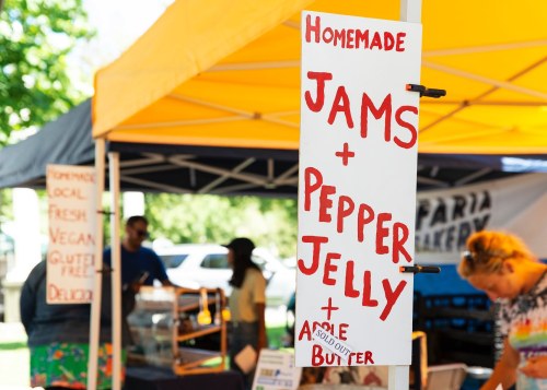 Sign at a market stall advertising homemade jams, pepper jelly, and apple butter under a yellow tent.