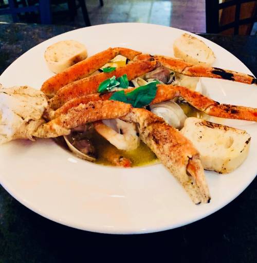 A plate of seafood featuring crab legs, shrimp, and seasoned vegetables, garnished with fresh basil.