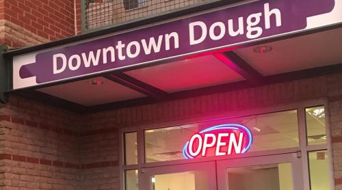 Sign for "Downtown Dough" with a bright "OPEN" neon light in the window.