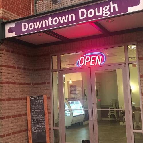 Exterior of Downtown Dough shop with an "OPEN" sign and menu displayed in the window. Bright and inviting atmosphere.