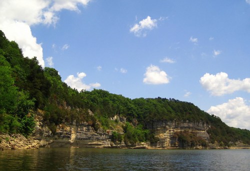 A serene landscape featuring rocky cliffs and lush greenery under a blue sky with scattered clouds.